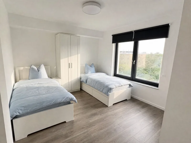 Zweibettzimmer mit hellblauer Bettwäsche und Fenster zum Grünen